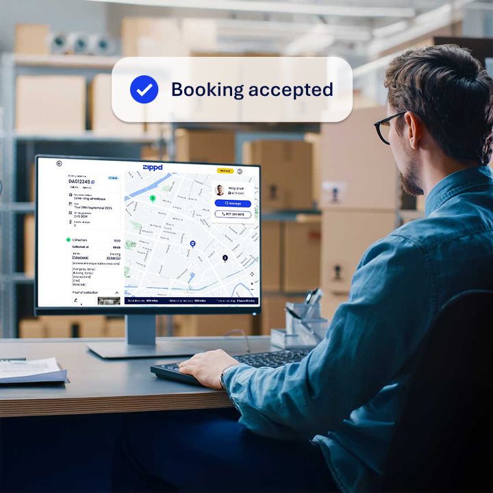 An image showing a person, sitting at a desk using a desktop computer. The computer screen shows the Zippd tracking page with the driver's live location on the screen. Overlayed is a Booking Accepted notification